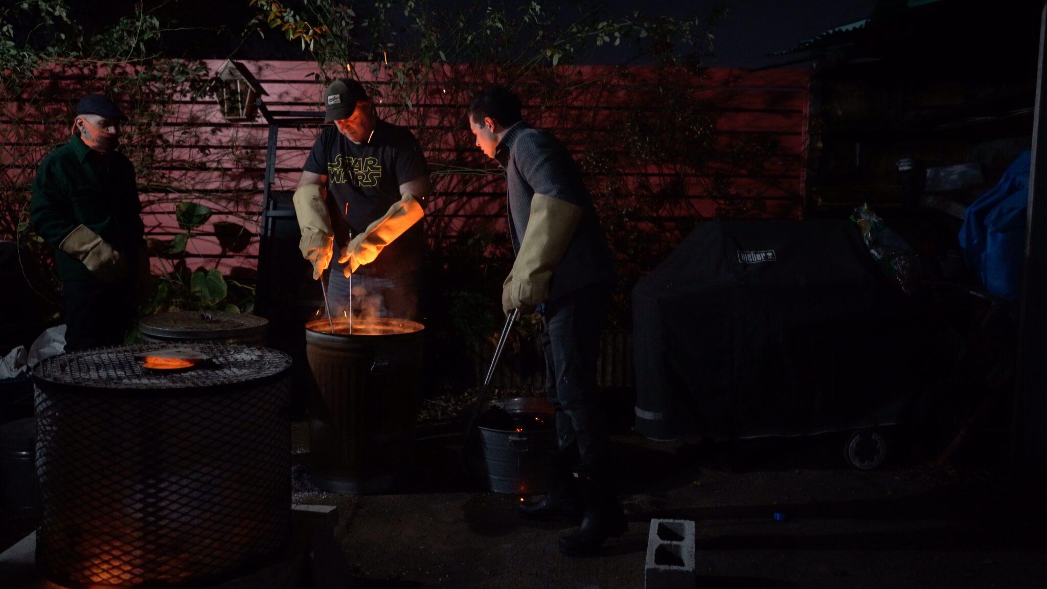 A photograph of Andrew Cornell Robinson (center) working with artists Jeffrey Goldstein (left) and Alonso Cartú (right) firing a western-style Raku Kiln.