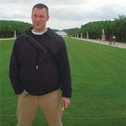 Color photograph of visual artist Andrew Cornell Robinson standing in the gardens of the Palace of Versailles