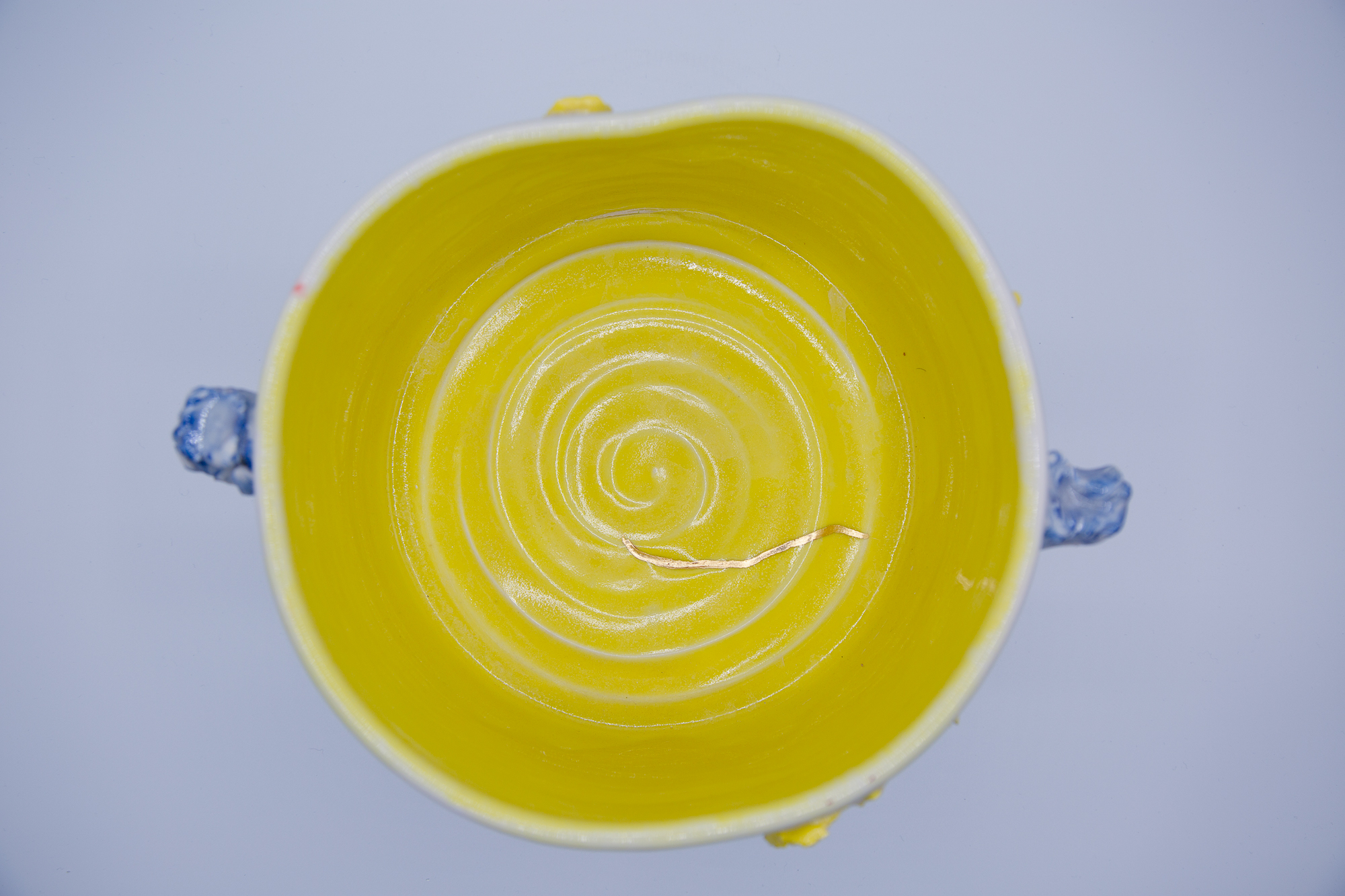 Photograph of a wheel thrown bowl made of porcelain with a yellow interior, and colored agate ware applique with a clear glaze, and gold leaf.