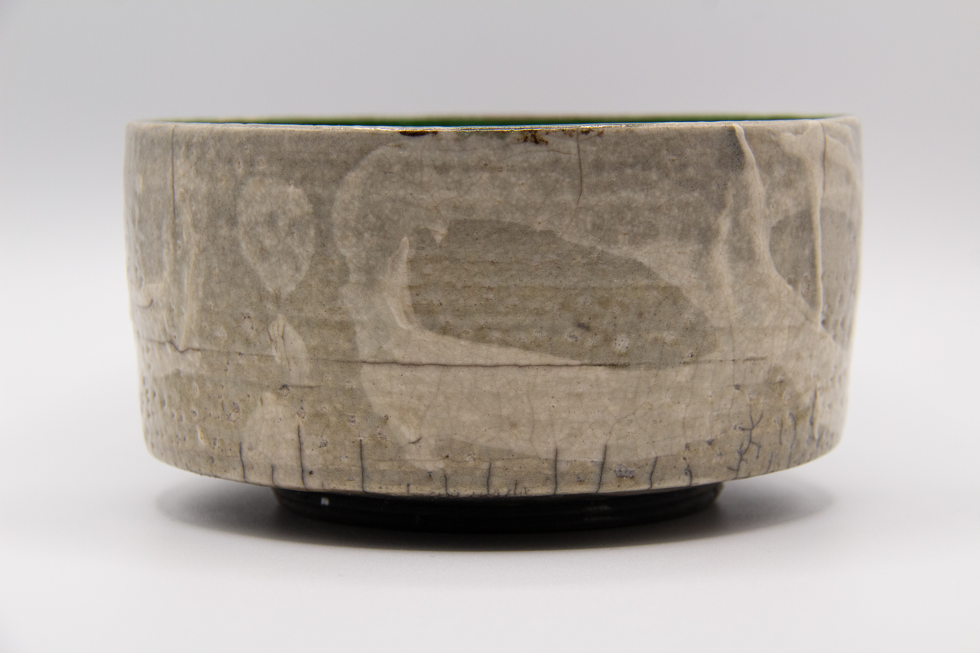 A photograph of a raku fired copper green and clear glazed footed tea bowl with a crackled surface and white slip decoration on the surface by Andrew Cornell Robinson