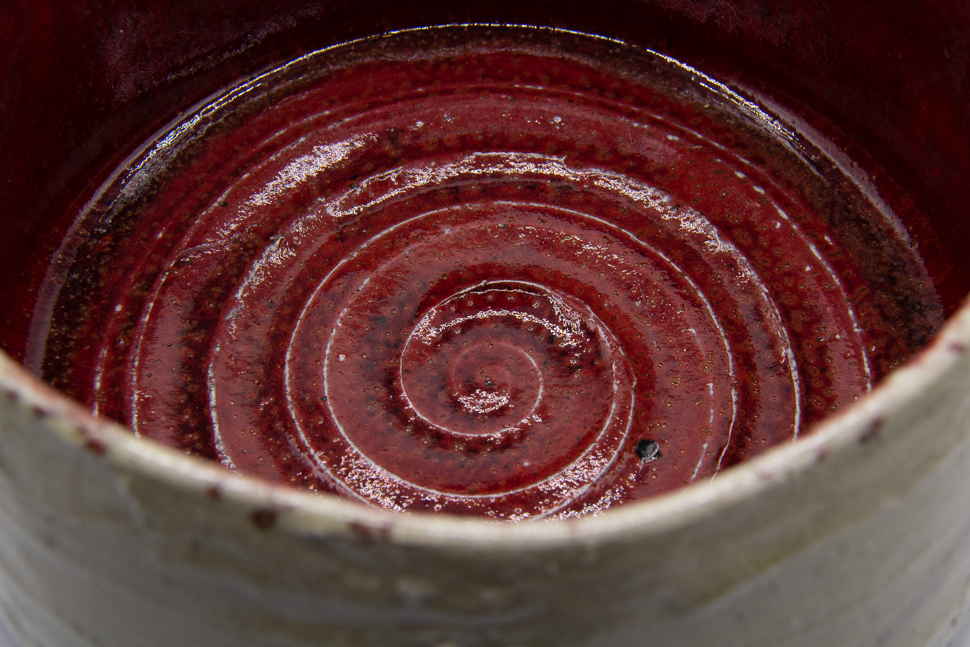 A photograph of a raku fired red and clear glazed footed tea bowl with a crackled surface and white slip decoration on the surface by Andrew Cornell Robinson
