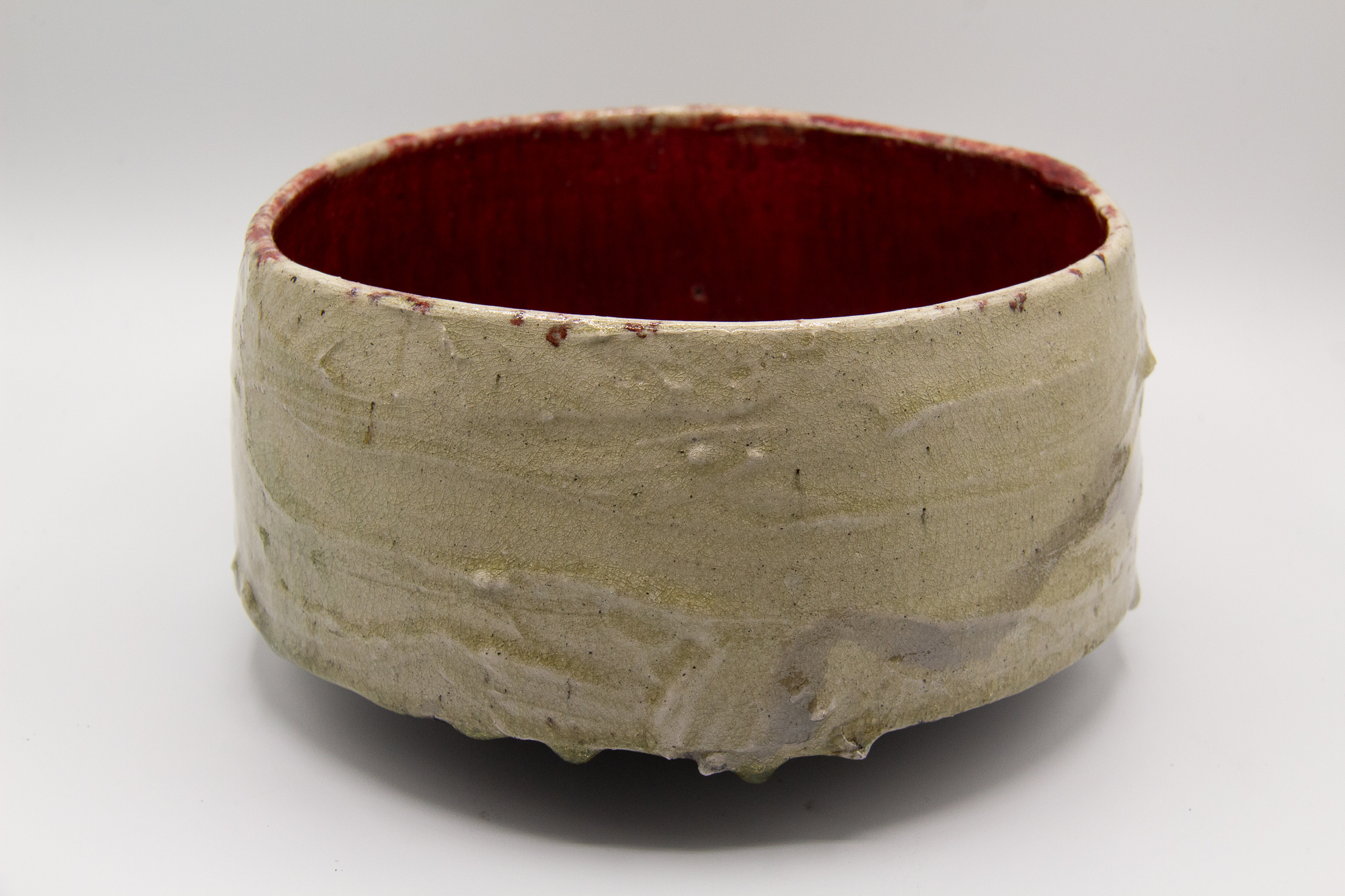 A photograph of a raku fired red and clear glazed footed tea bowl with a crackled surface and white slip decoration on the surface by Andrew Cornell Robinson