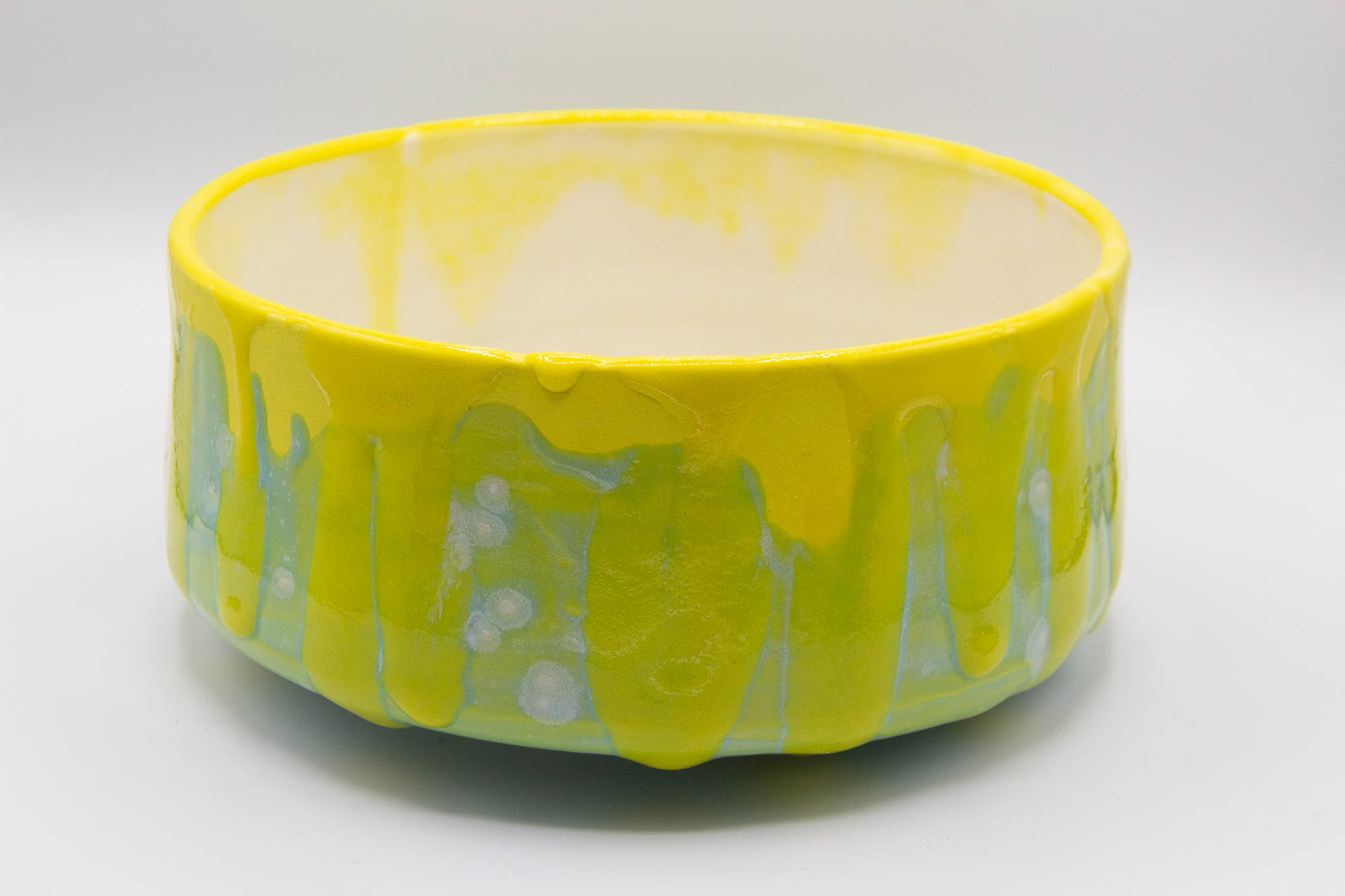 Photograph of a wheel thrown bowl made of porcelain with a yellow and green crystal and celadon glazes.