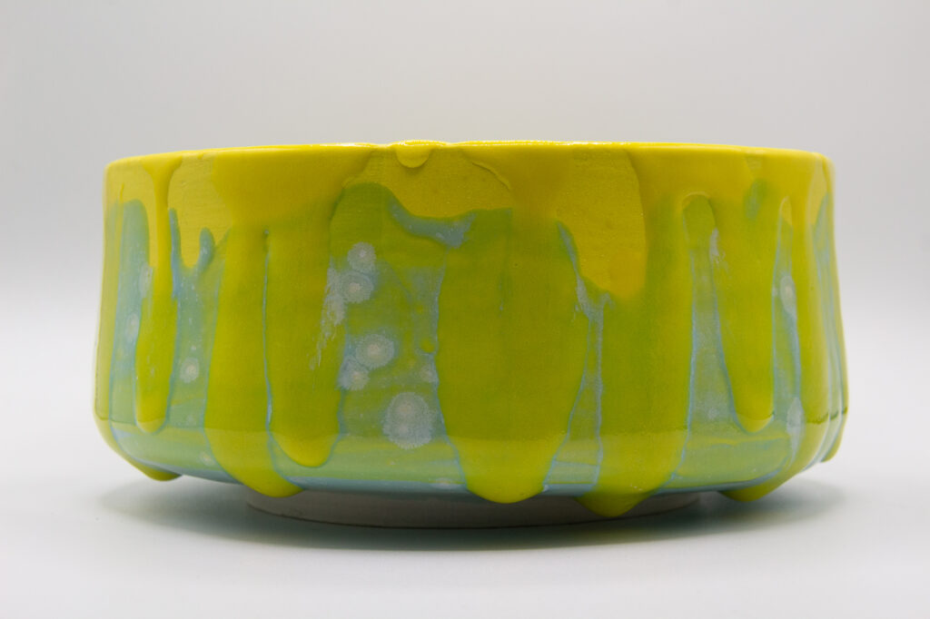 Photograph of a wheel thrown bowl made of porcelain with a yellow and green crystal and celadon glazes.