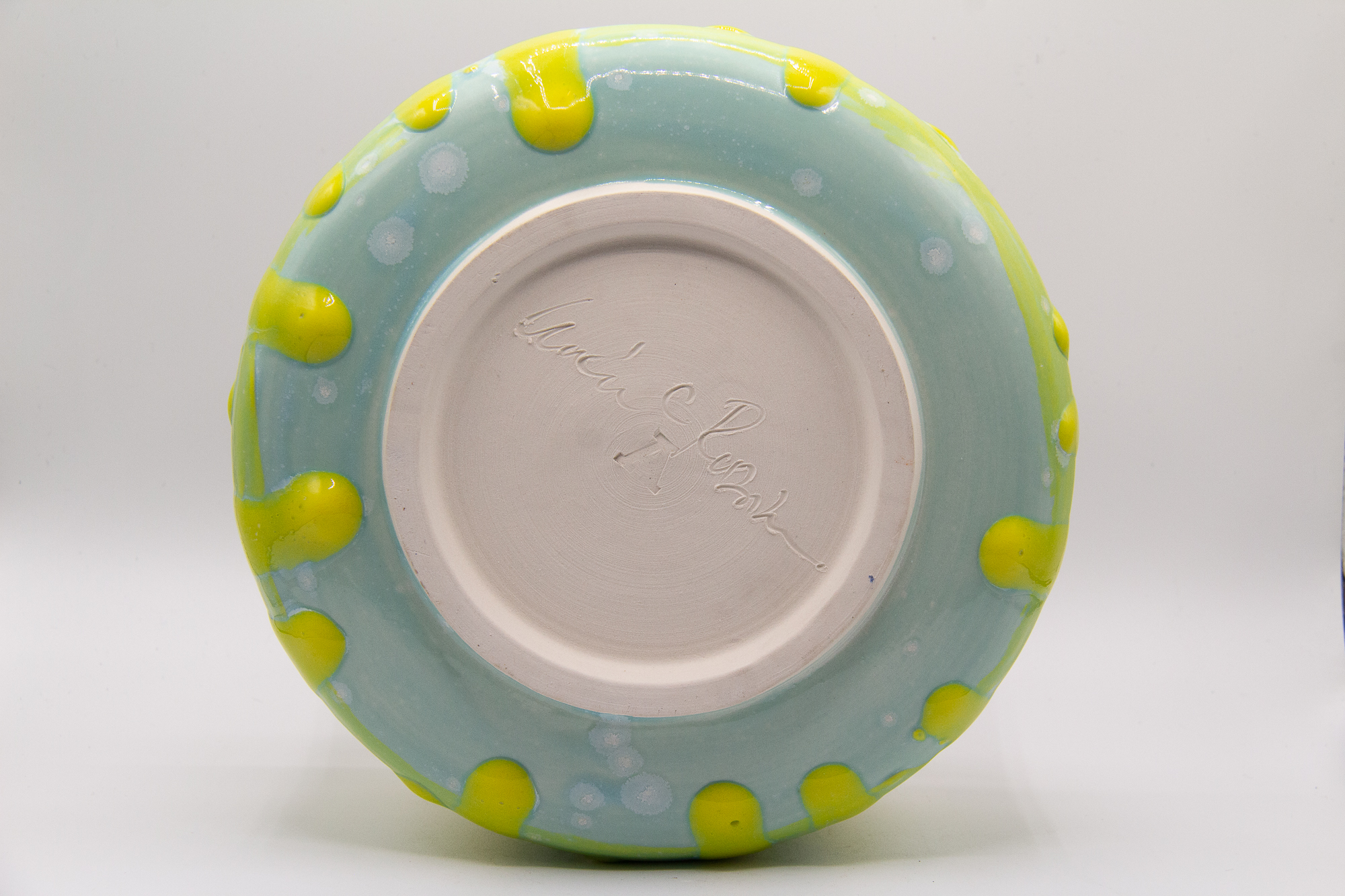 Photograph of a wheel thrown bowl made of porcelain with a yellow and green crystal and celadon glazes.